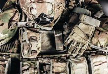 Capacete camuflado e luvas sobre equipamento militar, representando preparação tática.