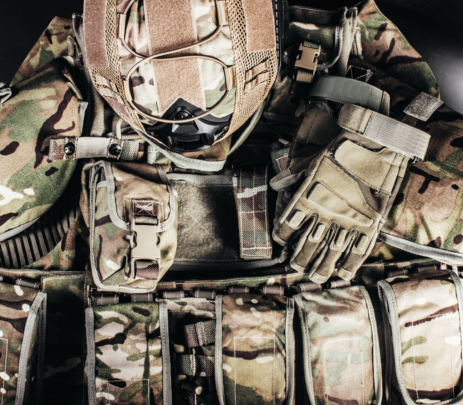 Capacete camuflado e luvas sobre equipamento militar, representando preparação tática.