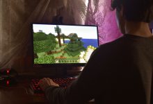 Jogador concentrado diante de um computador enquanto joga videogame em ambiente interno.