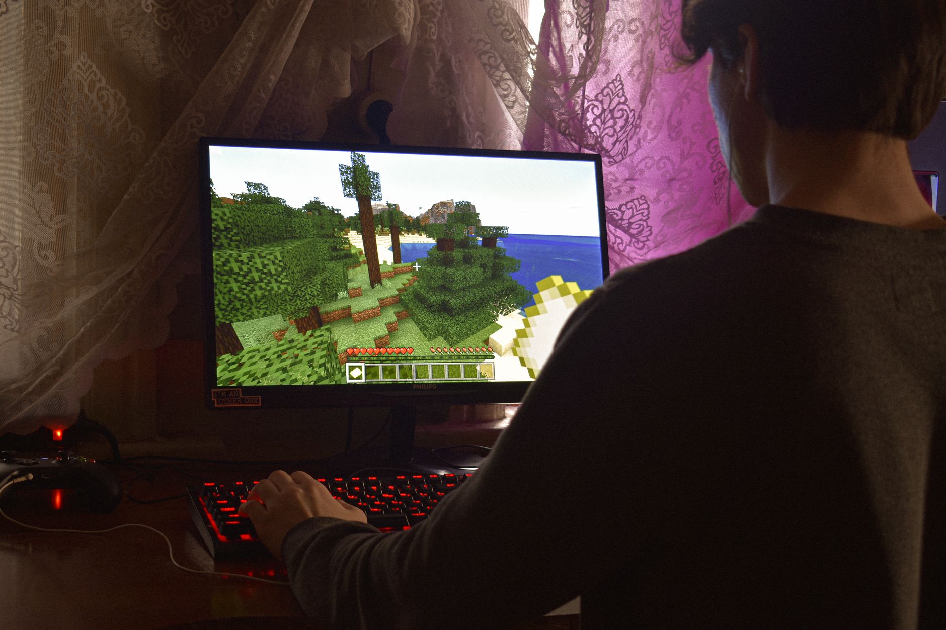 Jogador concentrado diante de um computador enquanto joga videogame em ambiente interno.