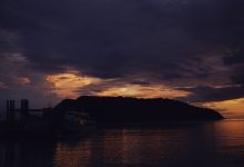 Barcos em silhueta diante de uma ilha durante o entardecer no mar.