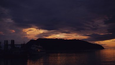 Barcos em silhueta diante de uma ilha durante o entardecer no mar.