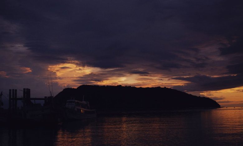 Barcos em silhueta diante de uma ilha durante o entardecer no mar.