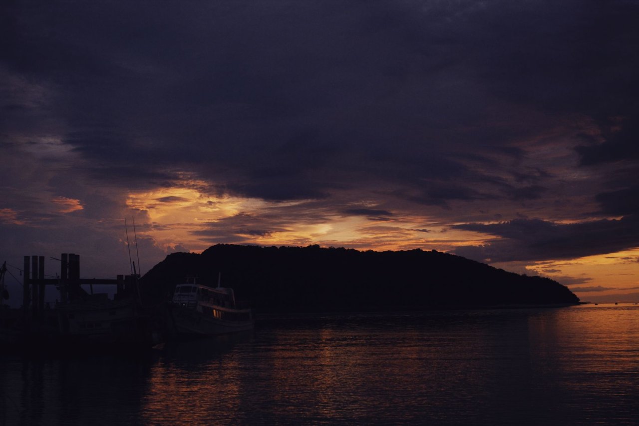 Barcos em silhueta diante de uma ilha durante o entardecer no mar.