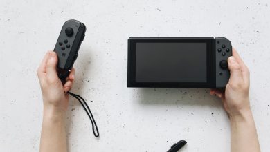 Mãos seguram um Nintendo Switch e controles Joy-Con sobre uma superfície branca.