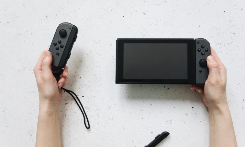 Mãos seguram um Nintendo Switch e controles Joy-Con sobre uma superfície branca.