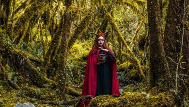 Mulher com capa vermelha segura um crânio em uma floresta densa e sombria.