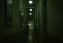 Corredor estreito e escuro de uma nave, iluminado por luzes verdes e luminárias suspensas.