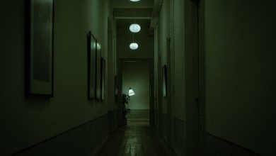 Corredor estreito e escuro de uma nave, iluminado por luzes verdes e luminárias suspensas.