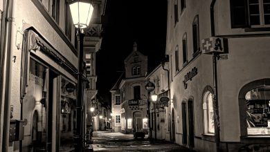 Rua de paralelepípedos entre prédios históricos, iluminada à noite.