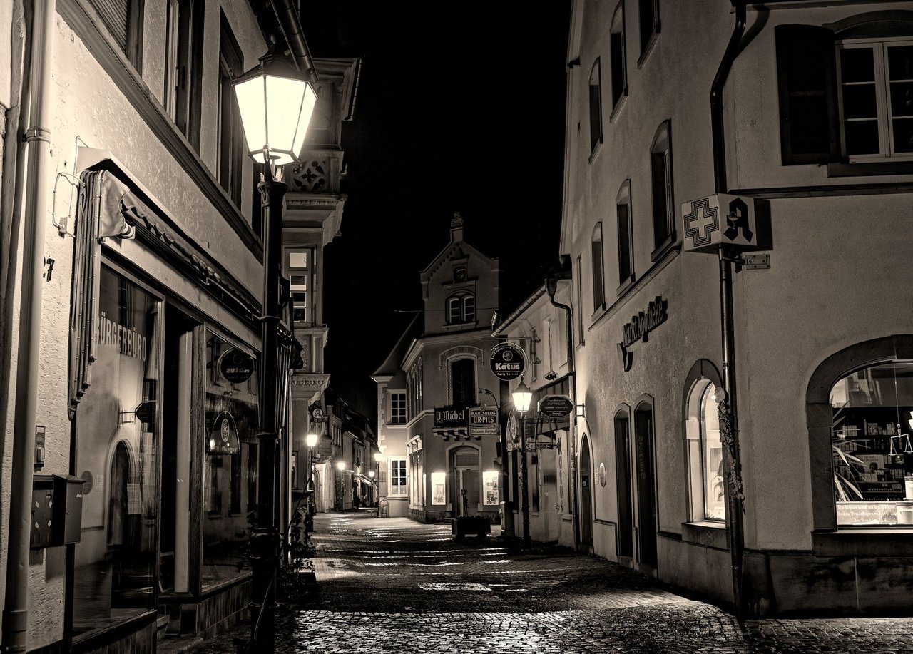 Rua de paralelepípedos entre prédios históricos, iluminada à noite.
