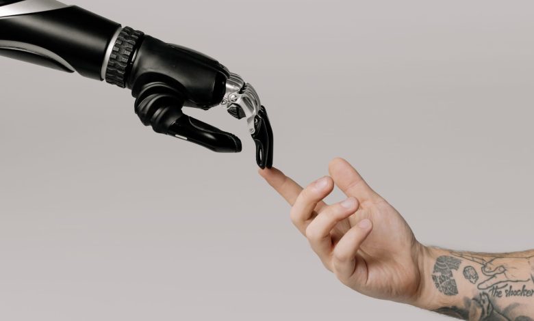 Mão humana tatuada se aproxima de uma mão robótica sobre fundo branco, simbolizando a relação entre humanos e inteligência artificial.
