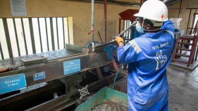 Trabalhador de macacão azul opera uma mesa vibratória para o processamento de minério em uma instalação industrial.