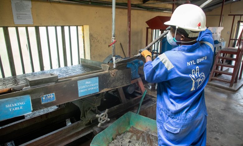 Trabalhador de macacão azul opera uma mesa vibratória para o processamento de minério em uma instalação industrial.