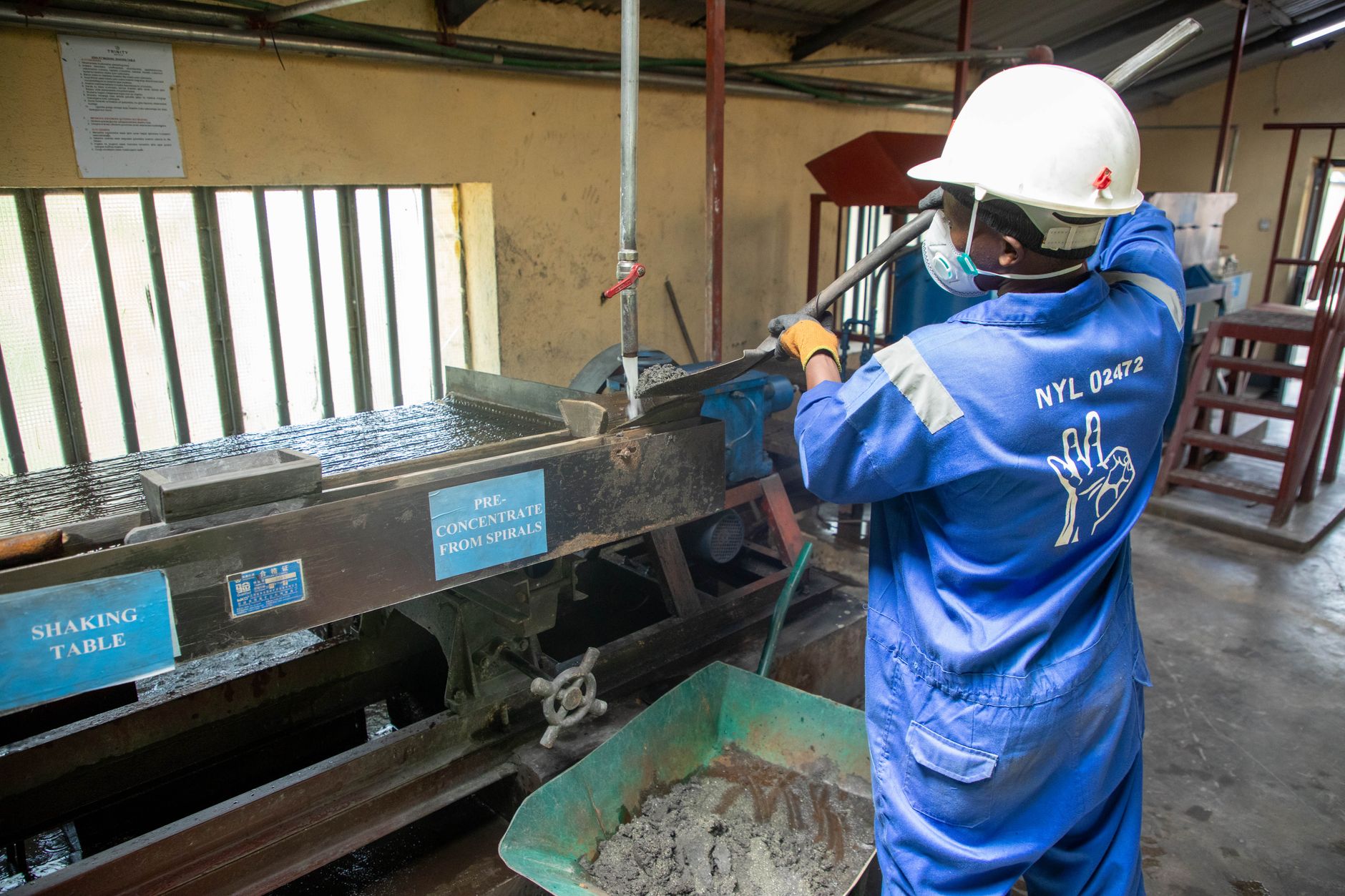 Trabalhador de macacão azul opera uma mesa vibratória para o processamento de minério em uma instalação industrial.
