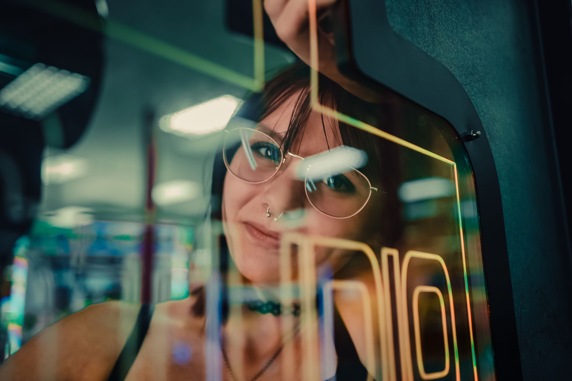 Mulher refletida no vidro de uma máquina de arcade, envolta por luzes neon.