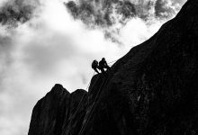 Escaladores sobem uma encosta rochosa íngreme diante de um céu nublado.