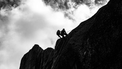 Escaladores sobem uma encosta rochosa íngreme diante de um céu nublado.